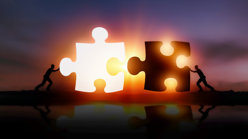 Two silhouettes pushing large puzzle pieces together at sunset, with the sun shining between the pieces.
