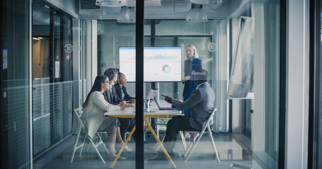Leaders meeting around a table while one person presents program results on a screen.