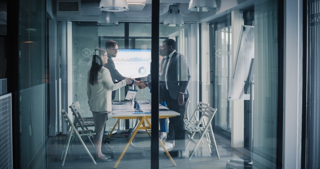 Colleagues shaking hands in a glass meeting room after a review.