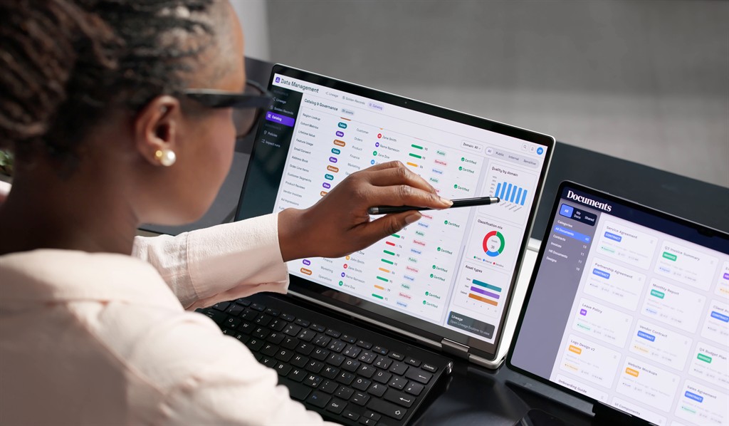 A person reviewing catalogs and documents on a laptop and tablet